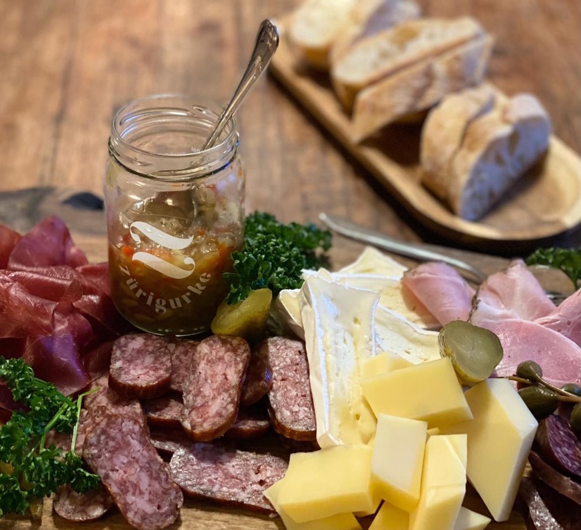 Ein Glas zuerigurke auf einer Platte mit Käse und Aufschnitt